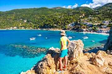 Female tourist standing among rocks and stones with Agios Nikitas beach in background, Lefkada island, Greece