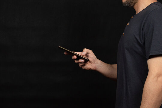 a man at the right side of the screen wearing a blue t shirt texting with a smartphone and a black background