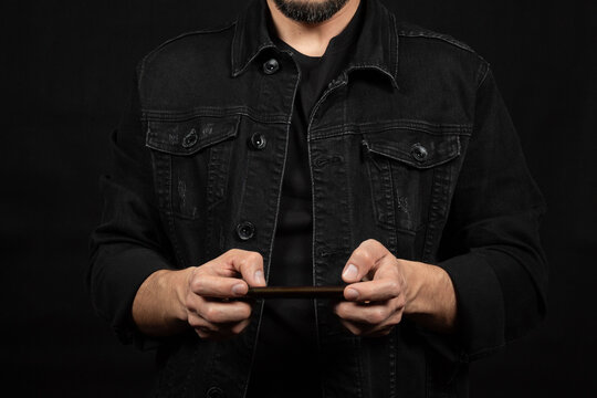 a man wearing a black denim jacket holding a smartphone in front of him - Powered by Adobe