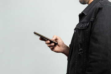 a man at the right side of the screen wearing a black denim jacket texting with a smartphone and a white background