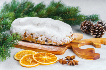 Traditional Christmas Stollen, sweet fruit loaf with sugar icing on wooden board and festive decor