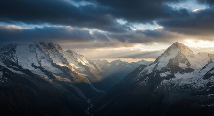 Dramatic light over snow-capped peaks in a mountain valley, rays through clouds