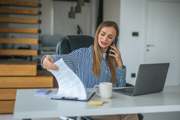 Businesswoman talking on phone and reviewing documents working from home