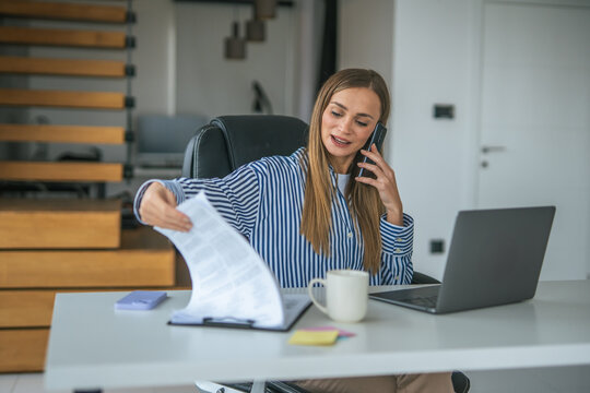 Businesswoman talking on phone and reviewing documents working from home