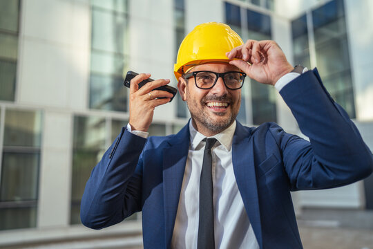 Happy engineer in suit talking on phone at construction