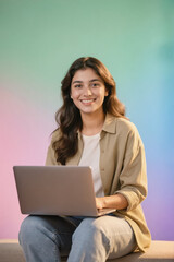 A smiling young woman with long brown hair using a laptop, seated against a colorful gradient background in a studio setting.
