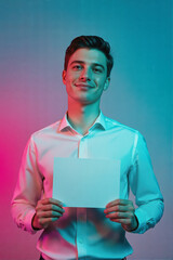 A young man in a white shirt holding an empty card against a vibrant pink and blue neon-lit background.