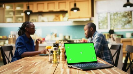 Chroma key display on laptop next to laughing couple enjoying morning routine together at the kitchen table. Man and woman drinking coffee, communication and household relaxation. Camera A. - Powered by Adobe