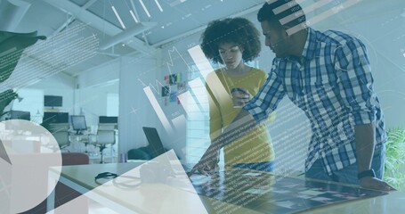 Leaning pair in yellow top and blue plaid shirt reviewing touchscreen in office with smartphone