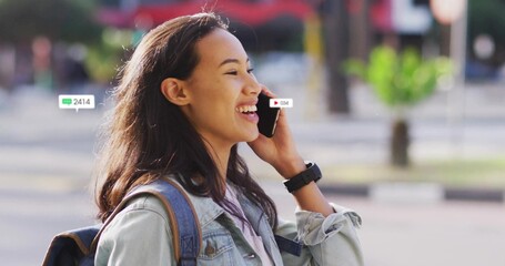 Talking Asian woman on smartphone at city plaza, wearing denim jacket, smartwatch, alert overlays