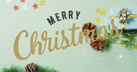 Showing gold Christmas script, black MERRY lettering on mint tabletop, with blue gift and pinecones