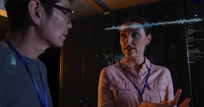 Gesturing woman in shirt with blue badge explaining servers in data center, waveform overlay