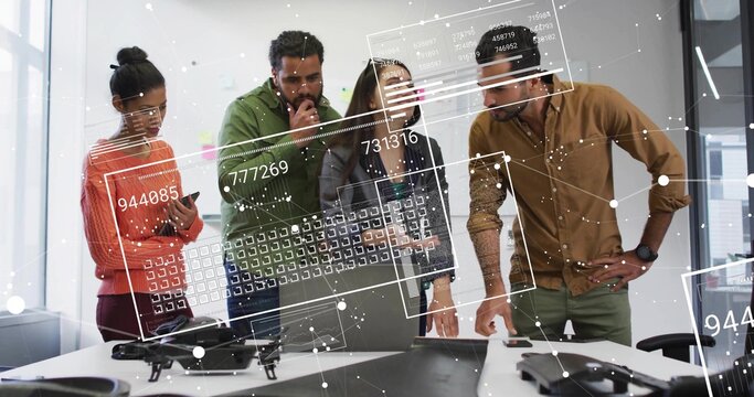 Reviewing team of six inspecting table in office, wearing jackets, with drone, laptop and overlays