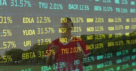 Standing male wearing red sports jersey raising hands on grass field with treeline, ticker overlay
