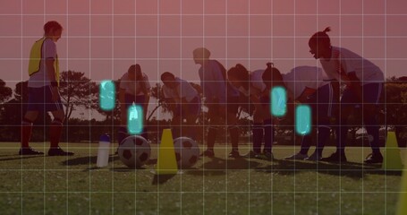 Practicing team and coach stretching on grassy pitch at sunset, with balls, cones, yellow bib, grid