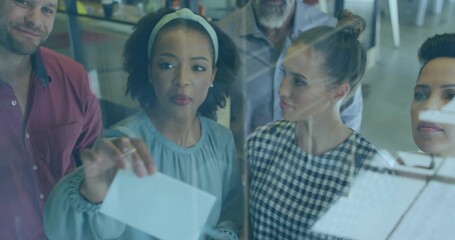 Placing leader woman in light blue blouse and headband, holding paper on glass board in office