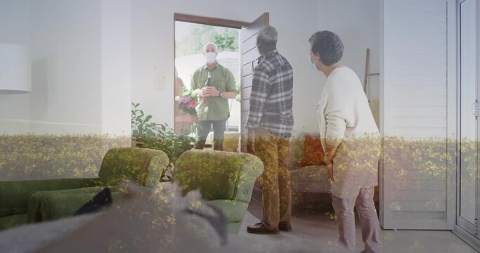 Holding bouquet, masked visitor in green shirt presenting package at front door, residents masked - Powered by Adobe