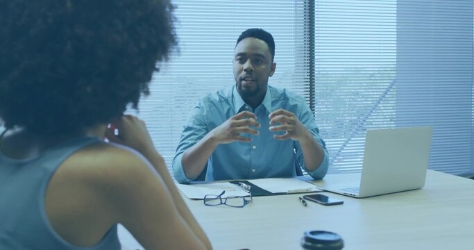 Gesturing manager wearing light blue shirt speaking at office meeting table, with laptop