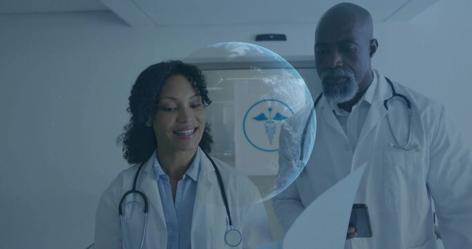 Reviewing two doctors studying charts at clinic, wearing lab coats stethoscope phone hologram globe - Powered by Adobe