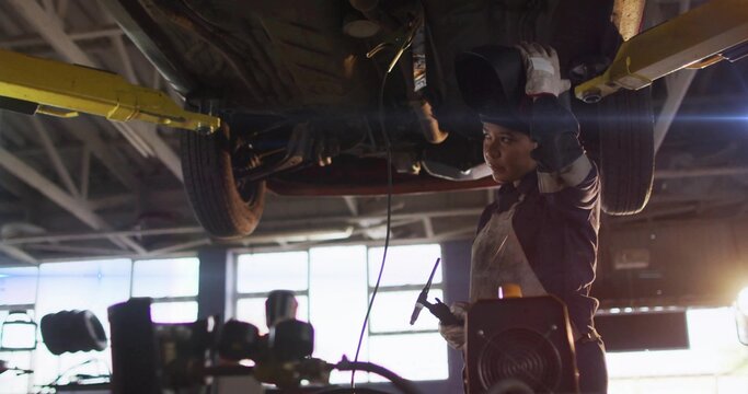 Welding tech wearing helmet gloves working under lifted car with torch on two-post lift, copy space
