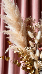 Elegant dried floral arrangement with pampas grass, golden eucalyptus, and bunny tails against pink curtain background
