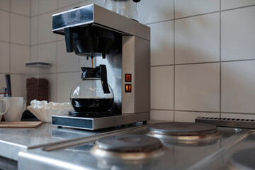 Active coffee maker with glass carafe positioned on kitchen counter showing brewing cycle in progress