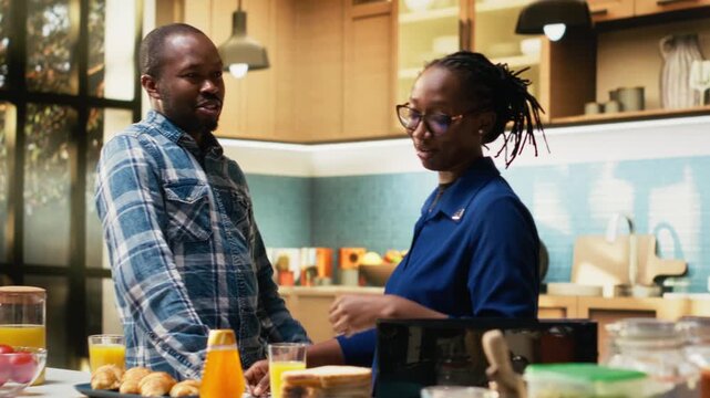 Boyfriend and girlfriend enjoying morning coffee and preparing fresh breakfast, bread and croissants. Cheerful couple shares togetherness, love and candid moments surrounded by good food. Camera B.