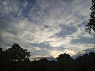 Fototapeta premium The image depicts a serene scene of a partly cloudy sky during either early morning or late evening, with the sun near the horizon casting a gentle glow.