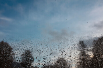 Water droplets scattered across windshield with blurred buildings and blue sky visible beyond