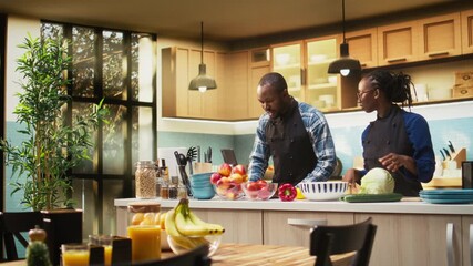 Black boyfriend and girlfriend preparing a meal with online food recipe on tablet, cutting ingredients and making a vegetarian salad in the kitchen, healthy lifestyle and culinary bonding. Camera A.
