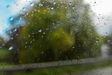 Water droplets on car window with soft blurred green trees in background