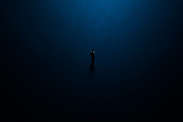 A lone figure stands dwarfed by an expansive, deep blue, mysterious backdrop, evoking feelings of profound solitude and contemplation within a vast, abstract space