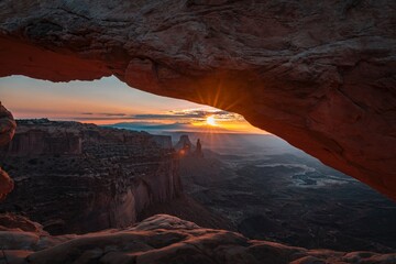 bryce canyon national park Displays a sunset viewed through a rocky arch. Full-frame composition, orange-blue tone. Realistic style, coastal background
