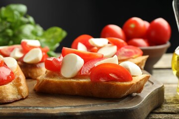 Tasty bruschettas with mozzarella cheese and tomatoes on wooden table against black background, closeup