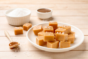 Tasty candies, salt and spoon with caramel sauce on light wooden table, closeup