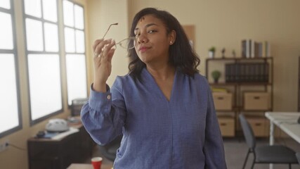 Woman holds glasses with fingertips near face before setting them aside in office building; confidence.