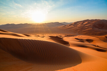 Rub' al-Khali (Empty Quarter) desert in Thumrayt, Dhofar, Oman, presenting sprawling orange sand dunes and a small settlement at the foot of distant hills under a clear morning sky © bennymarty
