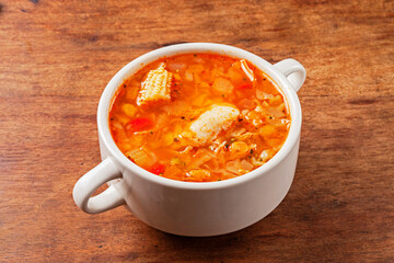 Italian tomato and chicken soup in a white bowl on a wooden background