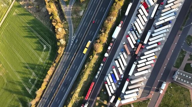 cargo yard overview, transport hub with organized trucks, overview of logistics area with trucks and greenery, high vantage shot of freight yard featuring vehicle alignment and surrounding