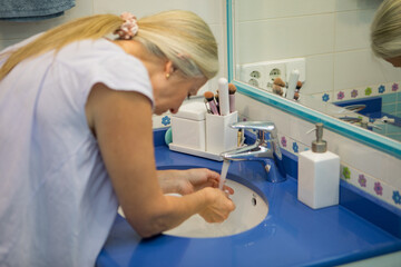 Washing hands at a bright blue sink in a cozy bathroom filled with simple decor and natural light
