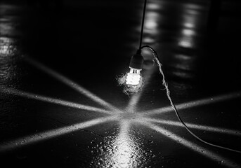 Dramatic black and white photo of a glowing compact fluorescent light bulb casting starburst rays on a wet floor.