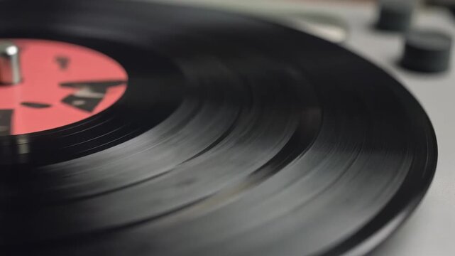 Close-up view of a black vinyl record spinning on a turntable with visible grooves and a red label.