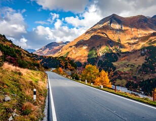 A winding road leads through a mountain pass in autumn, trees painted with the warm colors of fall