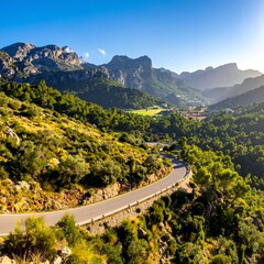 A winding road snakes through a green valley surrounded by rocky mountains under a clear blue sky
