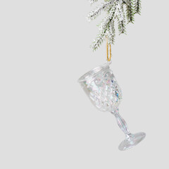 Minimal creative aesthetic view Glass of wine Christmas ornament hanging on snow fir branch on grey. New Year bright iridescent toy as wineglass. Minimal concept of celebrate, party, winter holidays.