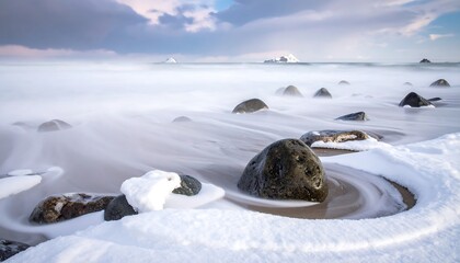 A winter seascape with snowy rocks and a long exposure blurring the ocean into a hazy fog-like texture