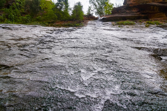 A low-angle view of a smooth rock face covered in flowing water along the Zion Narrows hike capturing texture, movement, and the beauty of the canyon environment
