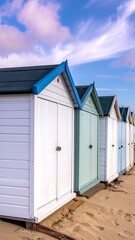 A row of colorful, gabled beach huts lines a sandy shore under a partly cloudy, blue sky at eye-level perspective