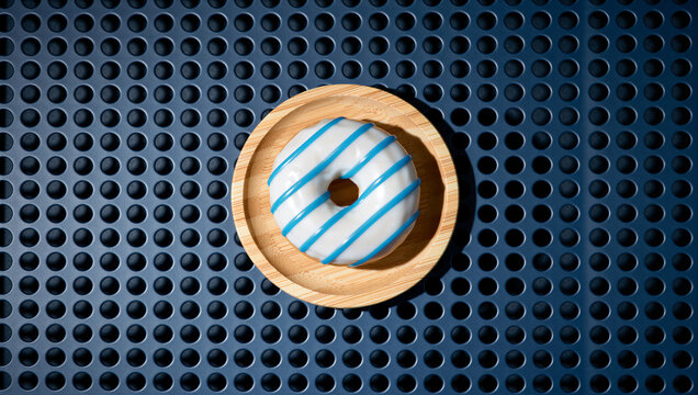 Overhead shot of a delicious donut with white frosting and blue stripes on a wooden plate