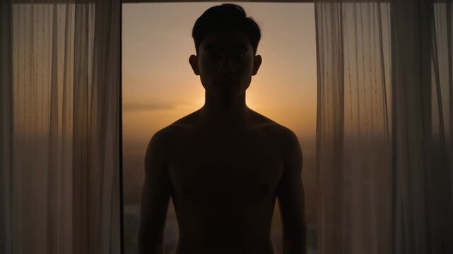 the silhouette of a shirtless man&nbsp;standing in front of a window, illuminated by the bright light of a rising or setting sun.&nbsp;Curtains on either side of the window provide contrast in the backlight.&nbsp;n